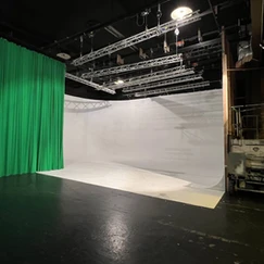 Studio de tournage avec un fond blanc, un fond vert sur le côté, et un ensemble complexe de lumières et de structures de support au plafond