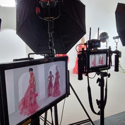 Équipement de prise de vue professionnel, comprenant un appareil photo numérique, des moniteurs affichant des images de modèles en robes roses, et un éclairage de studio avec des parapluies, dans un environnement blanc