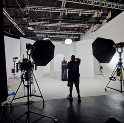 Vue en contre-jour d'un studio de photographie avec un photographe travaillant, entourés de grands éclairages à parapluie et d'équipements de caméra, mettant en scène une modèle féminine